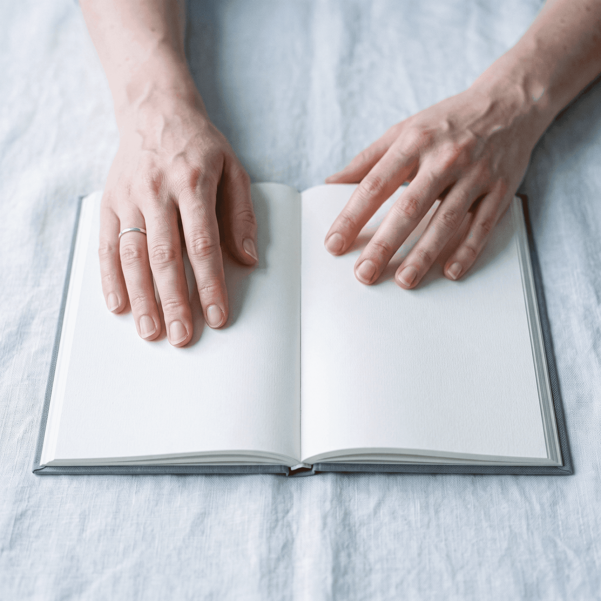 Two hands resting on an open, blank journal.